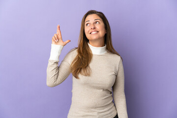 Middle age Brazilian woman isolated on purple background with fingers crossing and wishing the best