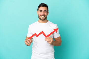 Young handsome caucasian man isolated on blue background holding a catching a rising arrow with happy expression