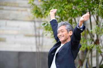 バンザイをして笑顔で喜ぶシニア男性　