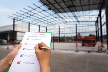 Action of an engineer is checking construction quality on the paperwork with warehouse building...