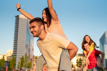 Generation z group of people having fun in the city, leisure activities with friends, two couple in piggyback style, city skyline background, freedom, happiness, carefree youth concepts