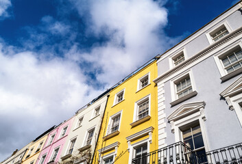 Fototapeta na wymiar Colourful terraced townhouses with summer sky background and space for text. The area of Notting Hill, London, is famous for streets of houses with brightly painted exteriors.