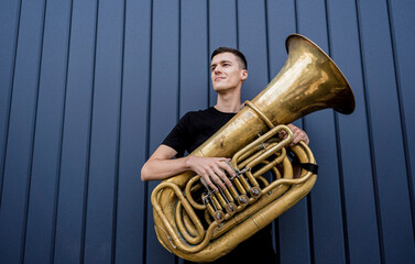 Young street musician playing the tuba near the big blue wall - obrazy, fototapety, plakaty