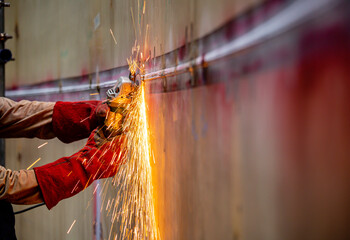 Worker using electric wheel spark grinding on welder metal carbon steel part shell plate inside tank