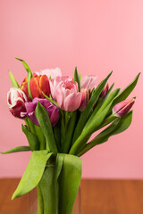 There are many beautiful multicolored tulips in a glass vase. A beautiful bouquet of tulips. Vertical banner