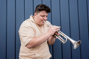Young street musician playing the trumpet near the big blue wall