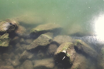 Disturbing cloudy water that reveals stones in a moment of tranquility with reflection of the sun