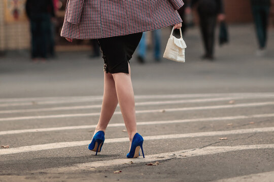 A woman in an oversized plaid jacket, black midi skirt and blue shoes in a European town. Stylish and confident business female walking down the street