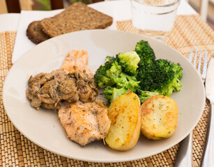 fried river trout fillet with a complex side dish of broccoli, baked potatoes and mushroom sauce