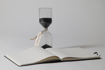 Hourglass with black sand, tied a note with an emotional phrase written "find time". Photographed in the studio on a white backdrop.