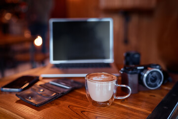 Traveler's breakfast. Cup of cappuccino on wooden table with laptop and photocamera.