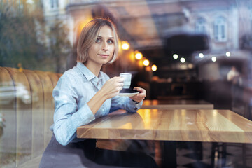 Drinking coffee. Pretty young woman holding cup of beverage while sitting at cafe.