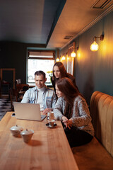 Coworking and freelance concept. Young  man  and two young women working together on laptop computer while sitting at cafe.