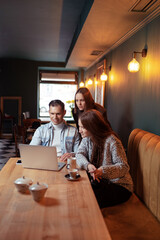 Fototapeta premium Coworking and freelance concept. Young man and two young women working together on laptop computer while sitting at cafe.