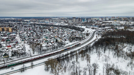View from a height of the winter city. The train rides on the railroad. Snow park. Cloudy winter day.