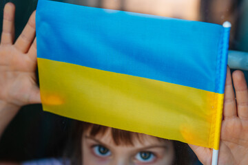 Little girl holding Ukrainian flag near the window