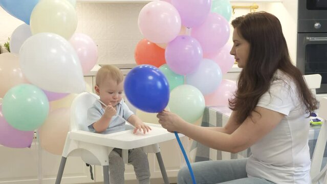 Mother and baby are preparing to celebrate children birthday blowing up balloons to decorate home for party. High quality 4k footage