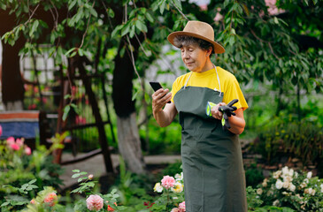 Senior woman gardener in a hat working in her yard and speaks on the phone. The concept of gardening, growing and caring for flowers and plants.