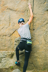 Young athletic woman in equipment doing rock climbing outdoors. Training area for outdoor activities. Extreme sport.