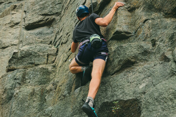 Young man in equipment doing rock climbing outdoors. Training area for outdoor activities. Extreme sport.