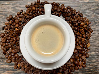 Golden espresso on white ceramic cup with coffee beans on wooden table closeup top view