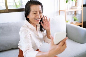 Middle age Asian woman holding cell telephone Work from home. smiling Beautiful mature asian woman...
