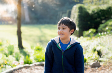 Happy young boy playing outdoor in the garden, Portrait Kid with smiling face enjoy playing outside in the morning , Child relaxing on sunny day Spring or Summer in the park.