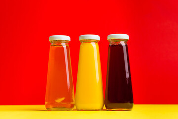 Bottles with yellow and red liquid halthy beverage on yellow and red background. Orange apple cherry