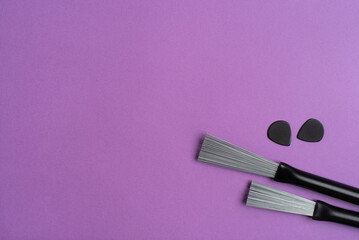 Drum brushes and guitar picks on a purple background. Flat lay, top view. 