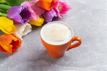 Spring multicolor tulips bouquet and cup of cappuccino on concrete background. Flowers and coffee