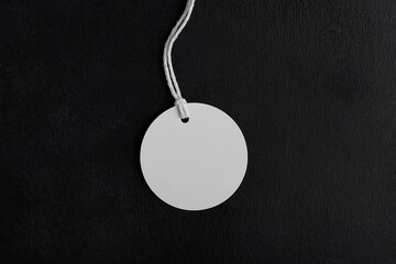 Round white tag label mockup with white cord, close up. Blank paper price tag isolated on black...