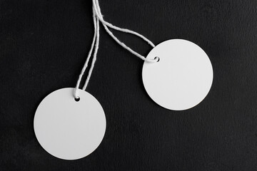 Two round white tag label mockups with white cord on black background. Blank paper circle price tags isolated, sale and black friday concept