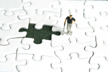 Miniature people toy figure photography. Winning tournament concept. A men golfer standing above missing puzzle jigsaw