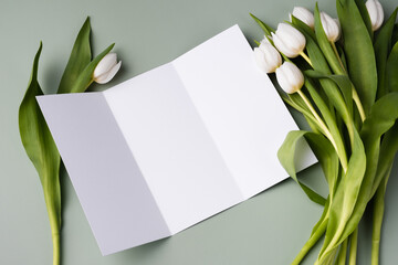 Mockup paper brochure on a pale green background with a bouquet of white beautiful tulips.