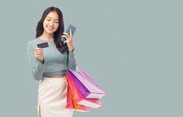 Young asian lady using mobile phone holding credit card carry shopping bags isolated over pastel...