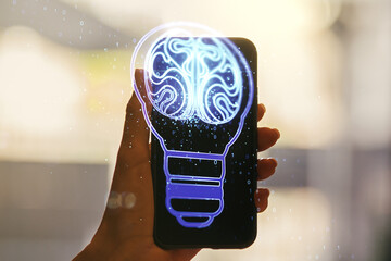 Double exposure of creative light bulb hologram with human brain and hand with cell phone on...