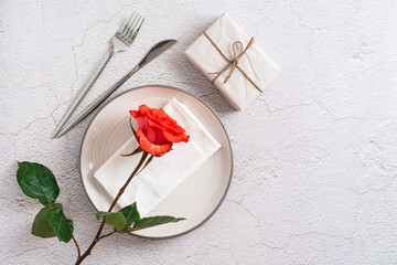 Plate, cutlery, gift and fresh red rose on a textured gray background. Eco holiday serving. Top view.