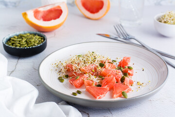 Fresh salad of grapefruit, clover and alfalfa sprouts and pumpkin seeds on a plate on the table....