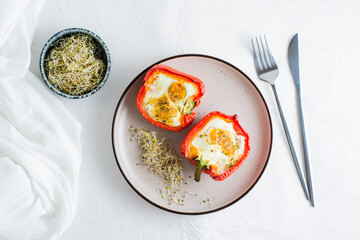 Bell pepper halves baked with egg and microgreens on a plate on the table. Flexitarian organic...