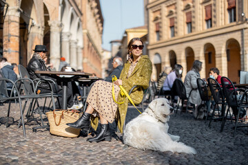 Stylish woman sitting with her white dog at outdoor cafe in the old town of Bologna city. Italian measured lifestyle and street fashion concept. Idea of traveling Italy © rh2010