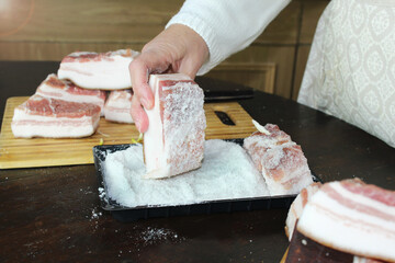 Close-up of the hand of a Caucasian elderly woman rolls lard in salt. Recipe for salting lard step by step. The cook prepares lard for salting