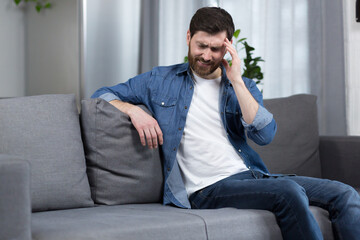 Fototapeta premium The man is at home, the patient is sitting on the couch, has a severe headache