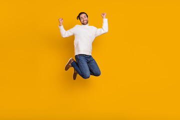 Fototapeta na wymiar Photo of cheerful lucky guy dressed white sweater rising fists jumping high isolated yellow color background