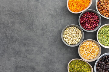 Different types of legumes in bowls, yellow and green peas and lentils, colored beans and maash, top view, copy space