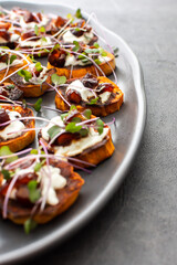 Oven baked slices of sweet orange sweet potato with yogurt and dates, sprinkled with microgreens, sweet potato on a gray oval ceramic dish