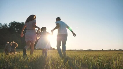 Happy family in park at sunset with pet. family has fun with child. Parents hold child by hands. Helping hand of parents. Walking happy family with pet in park at sunset.