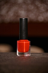 closeup the red color nail paint glass bottle with black cap over out of focus dark brown...