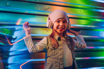 Little girl wearing headphones using smartphone on the colorful neon