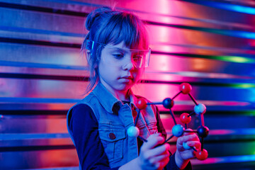 Little girl holding molecular model on the colorful neon background