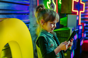 Little girl using tablet on the colorful neon background